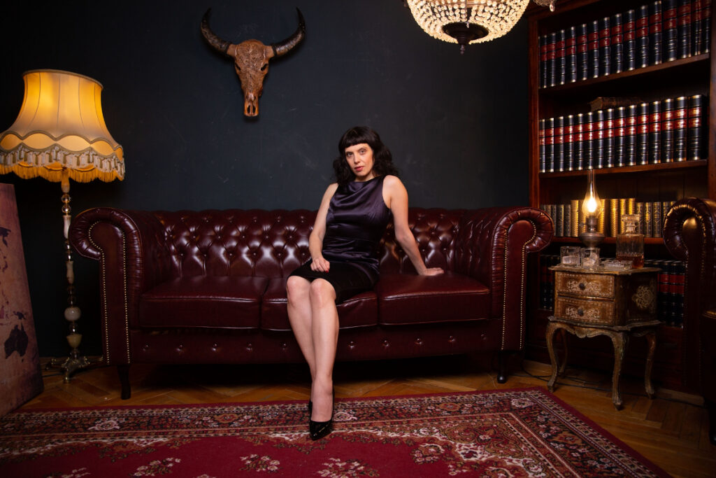 Berlin dominatrix Lady Vyra wearing a cocktail dress sitting on a leather couch