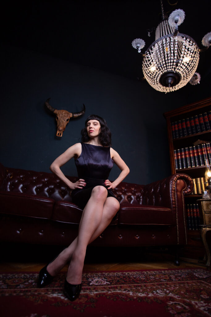 Berlin dominatrix Lady Vyra wearing a cocktail dress sitting on a leather couch