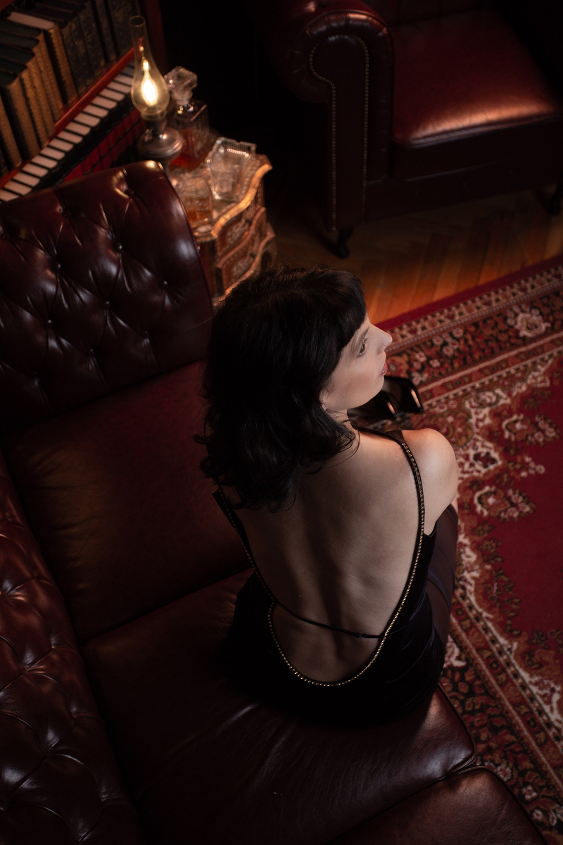 Berlin Dominatrix Lady Vyra elegantly dressed shows her bare back on a couch