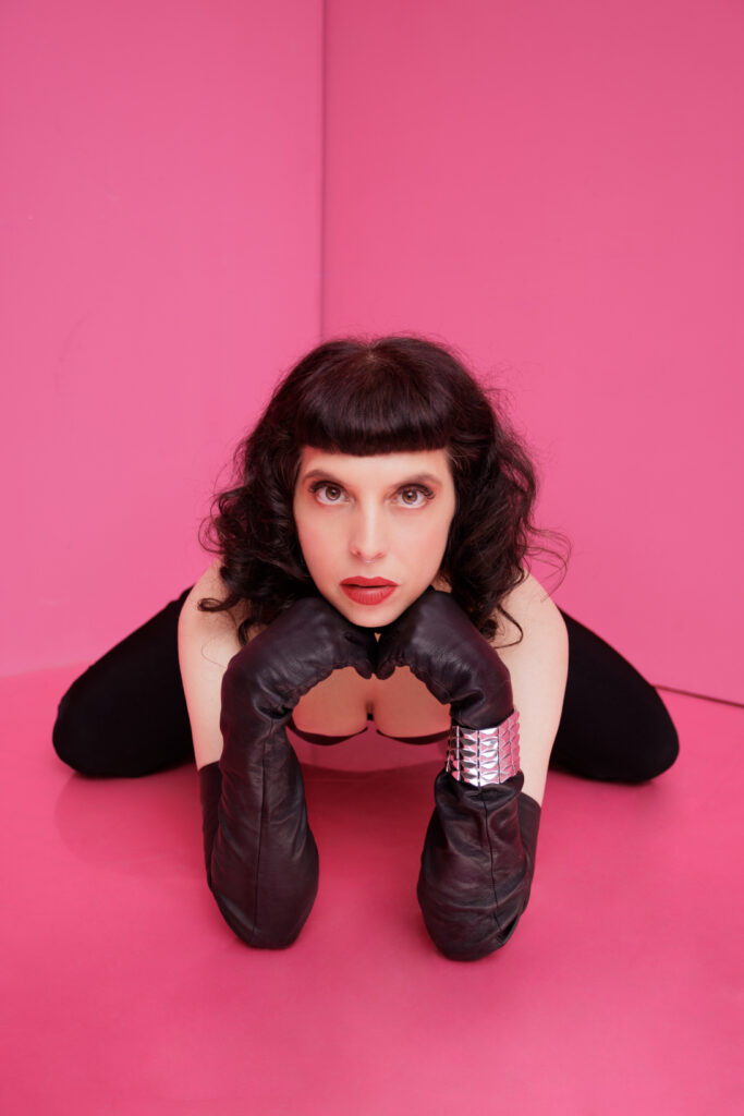 Berlin Dominatrix Lady Vyra in a leather corset and long leather gloves sitting on the floor looking deep into your eyes